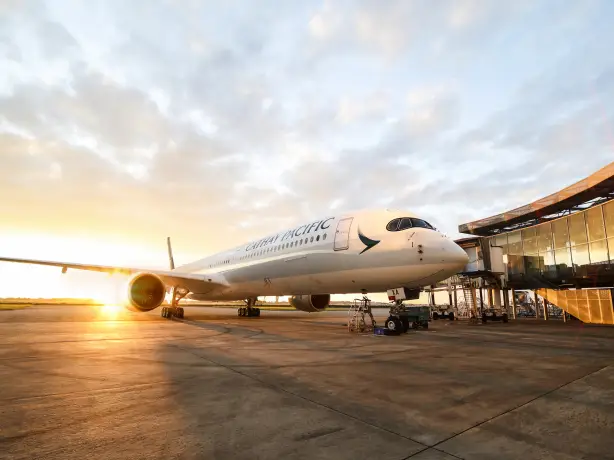 Ein Cathay Pacific Airbus am Flughafen mit einem Sonnenuntergang im Hintergrund.