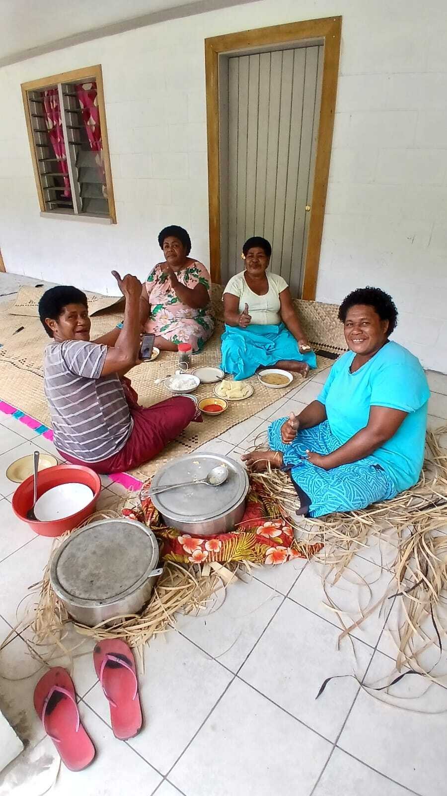 Een groep vrouwen zit op de grond en lacht naar de camera in het dorp Fiji