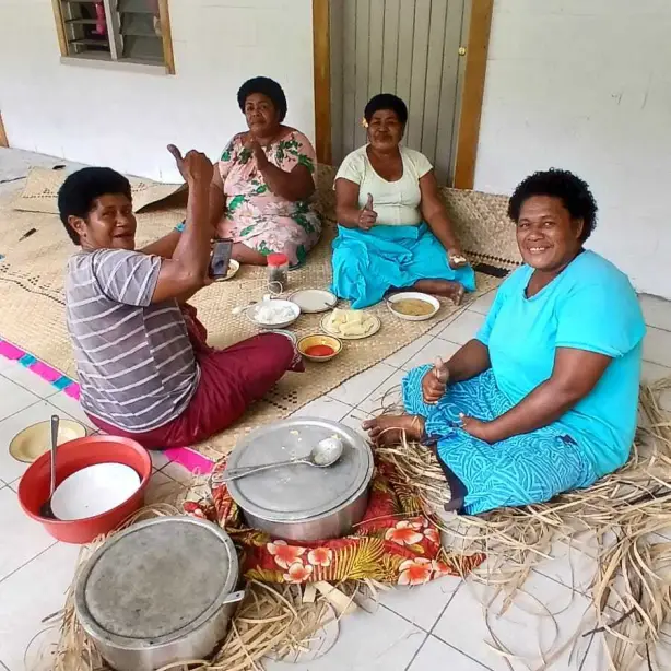 Een groep vrouwen zit op de grond en lacht naar de camera in het dorp Fiji