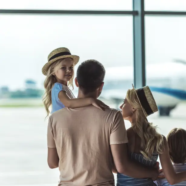 Een gezin met twee jonge kinderen dat vanuit het raam van een luchthaventerminal naar een vliegtuig op het platform kijkt, dat klaarstaat om op vakantie te vertrekken