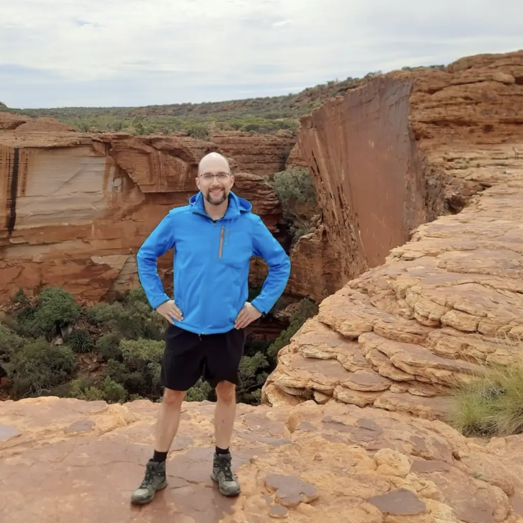 Mann mit blauer Jacke steht vor roter Felsenschlucht in Australien