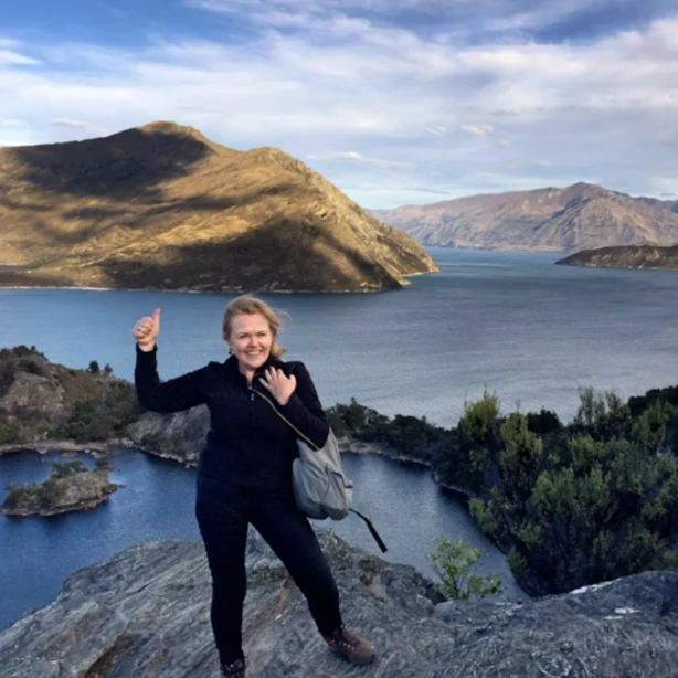 Gerrie glimlacht en geeft een duim omhoog naar de camera met de oceanen en bergen op de achtergrond