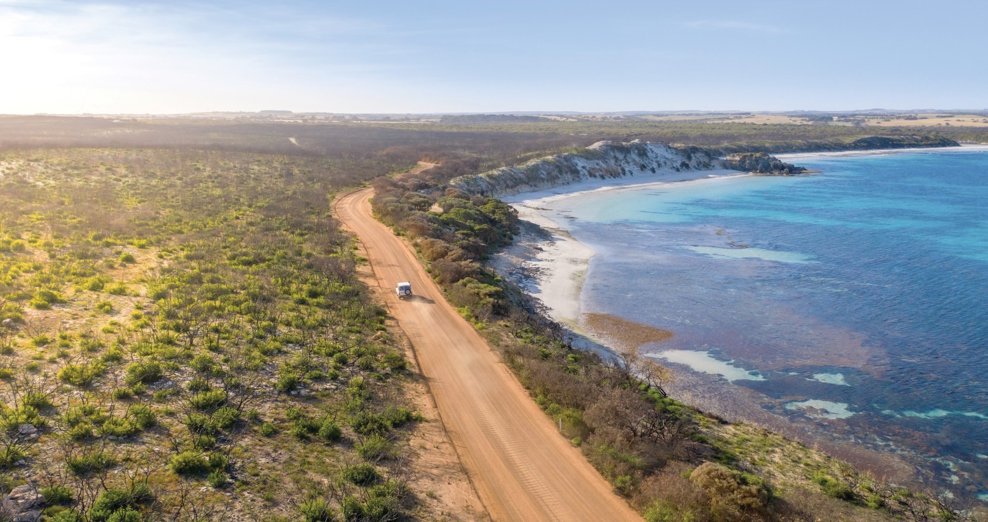 Luftaufnahme einer Küstenstraße auf Kangaroo Island, Australien, mit türkisfarbenem Meer, weißen Klippen und einem Fahrzeug, das an der Küste entlangfährt.