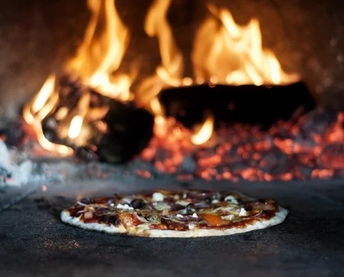 A pizza baking inside a wood fired oven