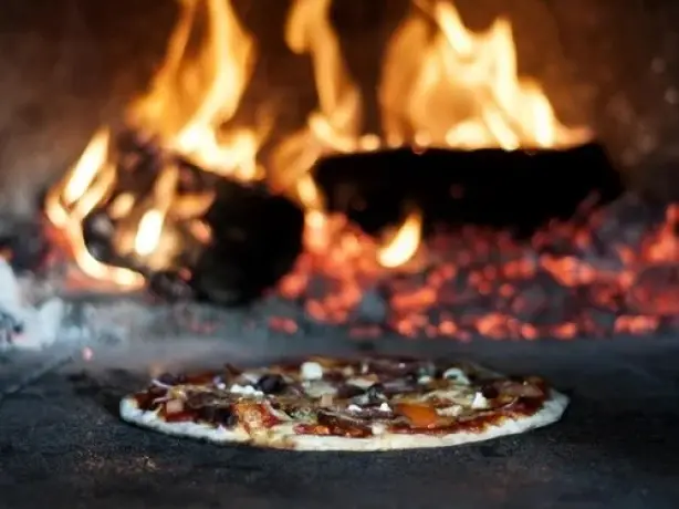 A pizza baking inside a wood fired oven