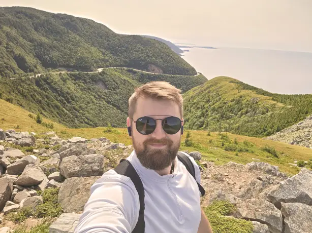 Luke, Travelessence Expert, taking a selfie with mountains and coast in the background