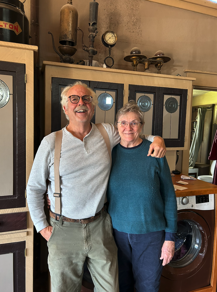 Smiling couple posing together inside a charming eclectic accommodation filled with vintage antiques and curios, local hosts welcoming guests in Canada