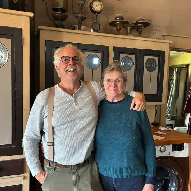 Een glimlachend stel dat samen poseert in een charmante, eclectische accommodatie vol vintage antiek en curiosa; lokale gastheren die gasten verwelkomen in Canada
