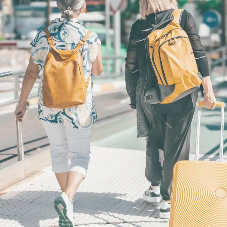 Two people walking to an airport wearing backpacks and one has a pull along suitcase