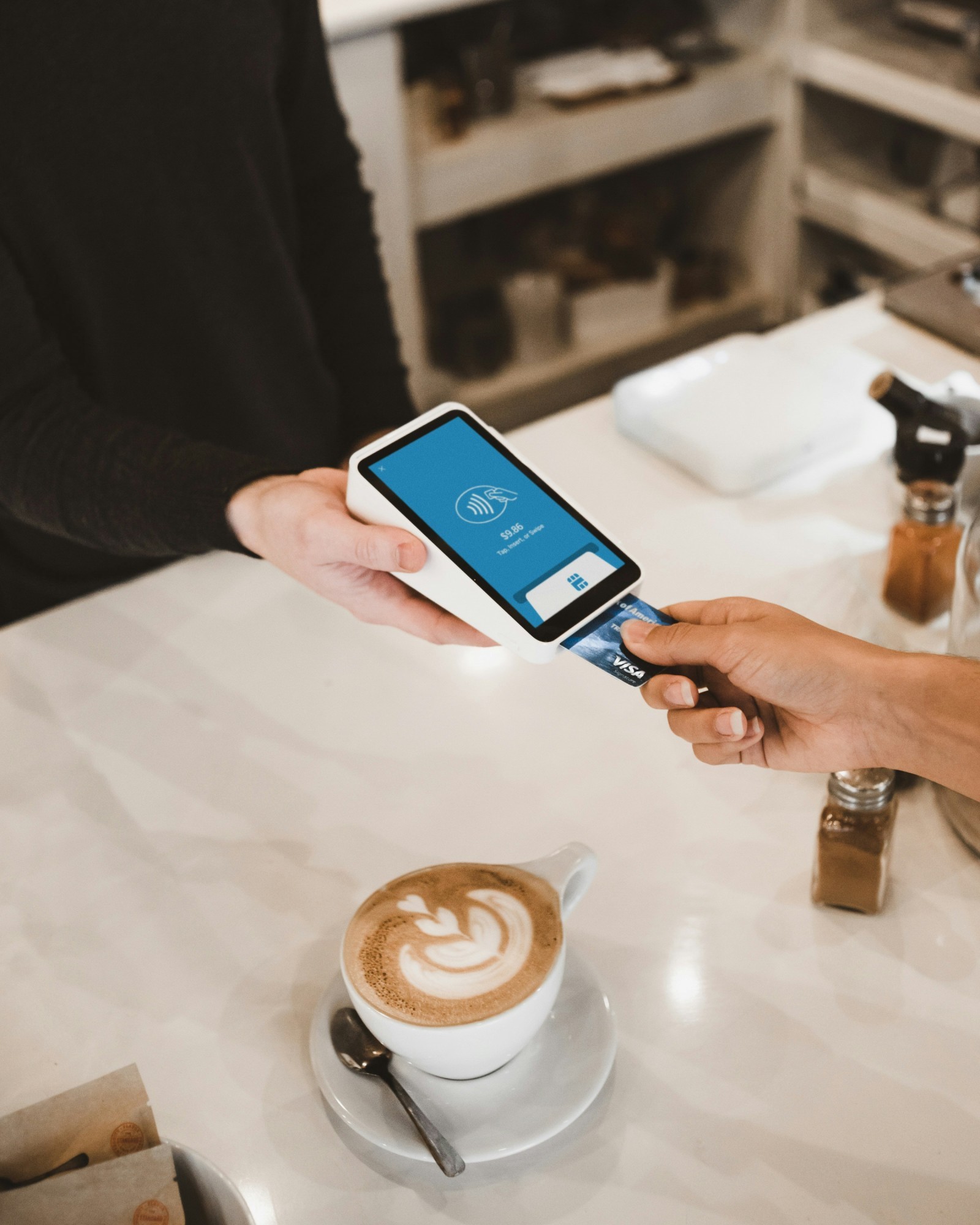 Person bezahlt mit Karte, unter ihr Kaffee am Tisch