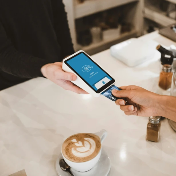 Person bezahlt mit Karte, unter ihr Kaffee am Tisch