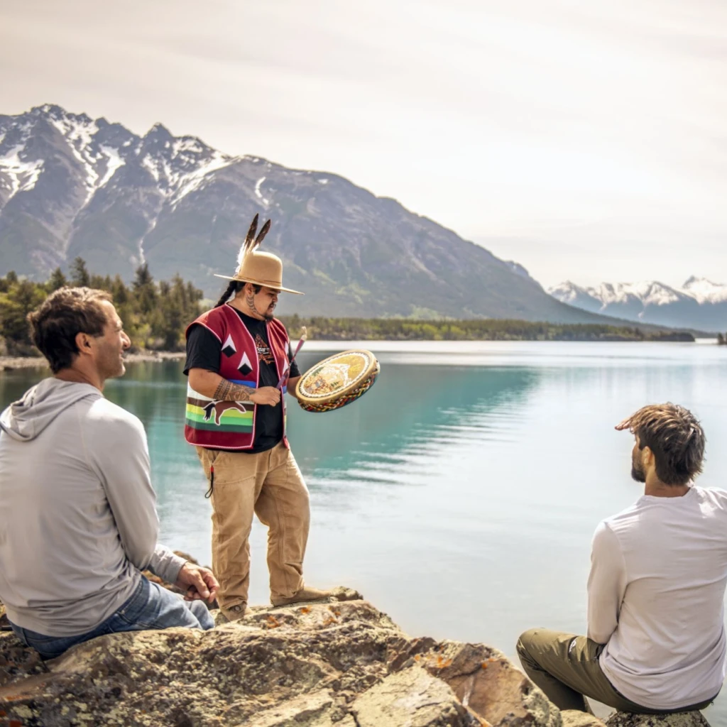 Een vader en zoon kijken naar een drumceremonie uitgevoerd door een inheemse gids bij Chilko Lake in British Columbia, Canada.