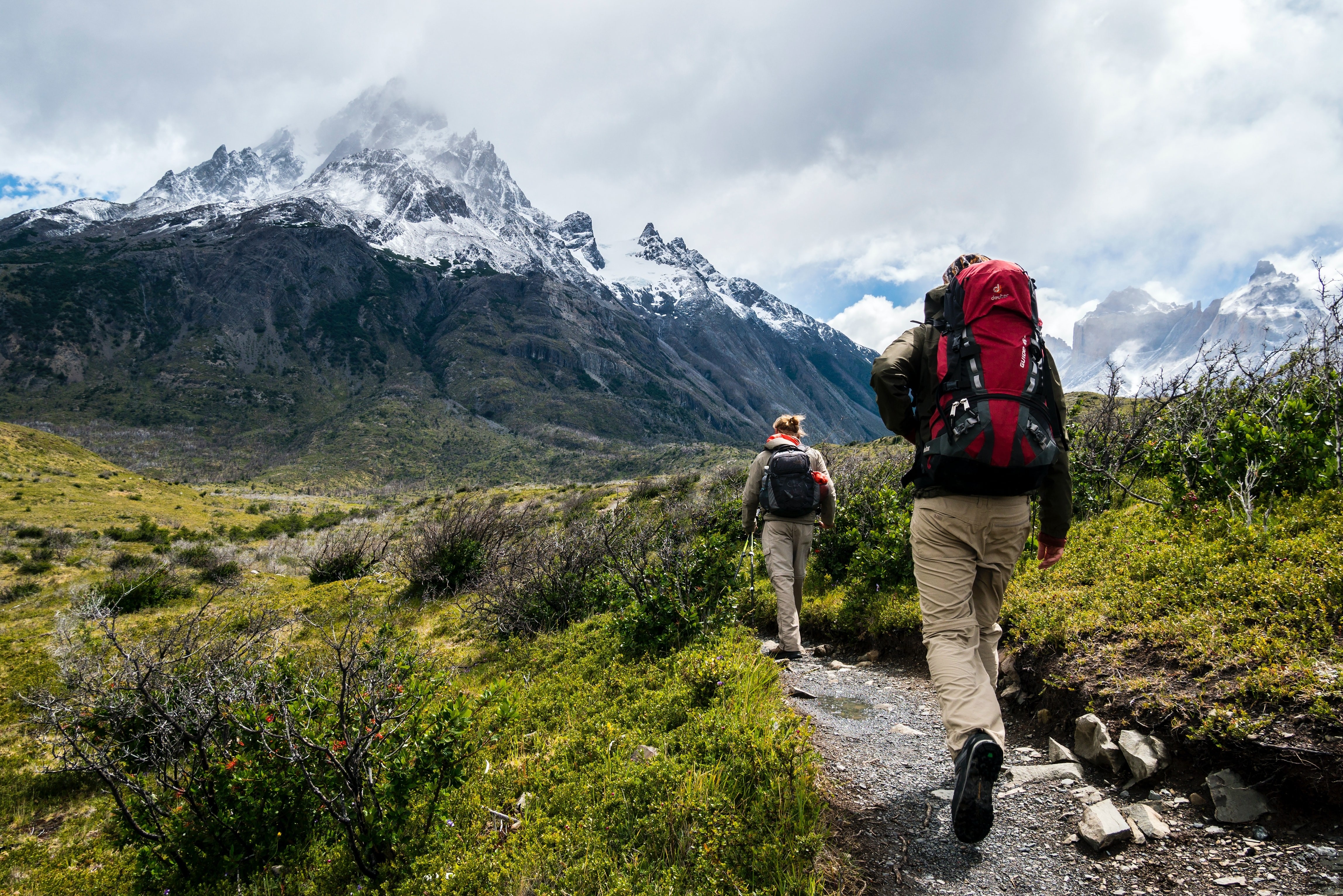 Zwei Wanderer auf dem Parker Ridge Trail in den kanadischen Rocky Mountains, mit schneebedeckten Bergen im Hintergrund und grüner Umgebung