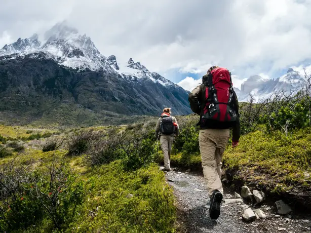 Zwei Wanderer auf dem Parker Ridge Trail in den kanadischen Rocky Mountains, mit schneebedeckten Bergen im Hintergrund und grüner Umgebung