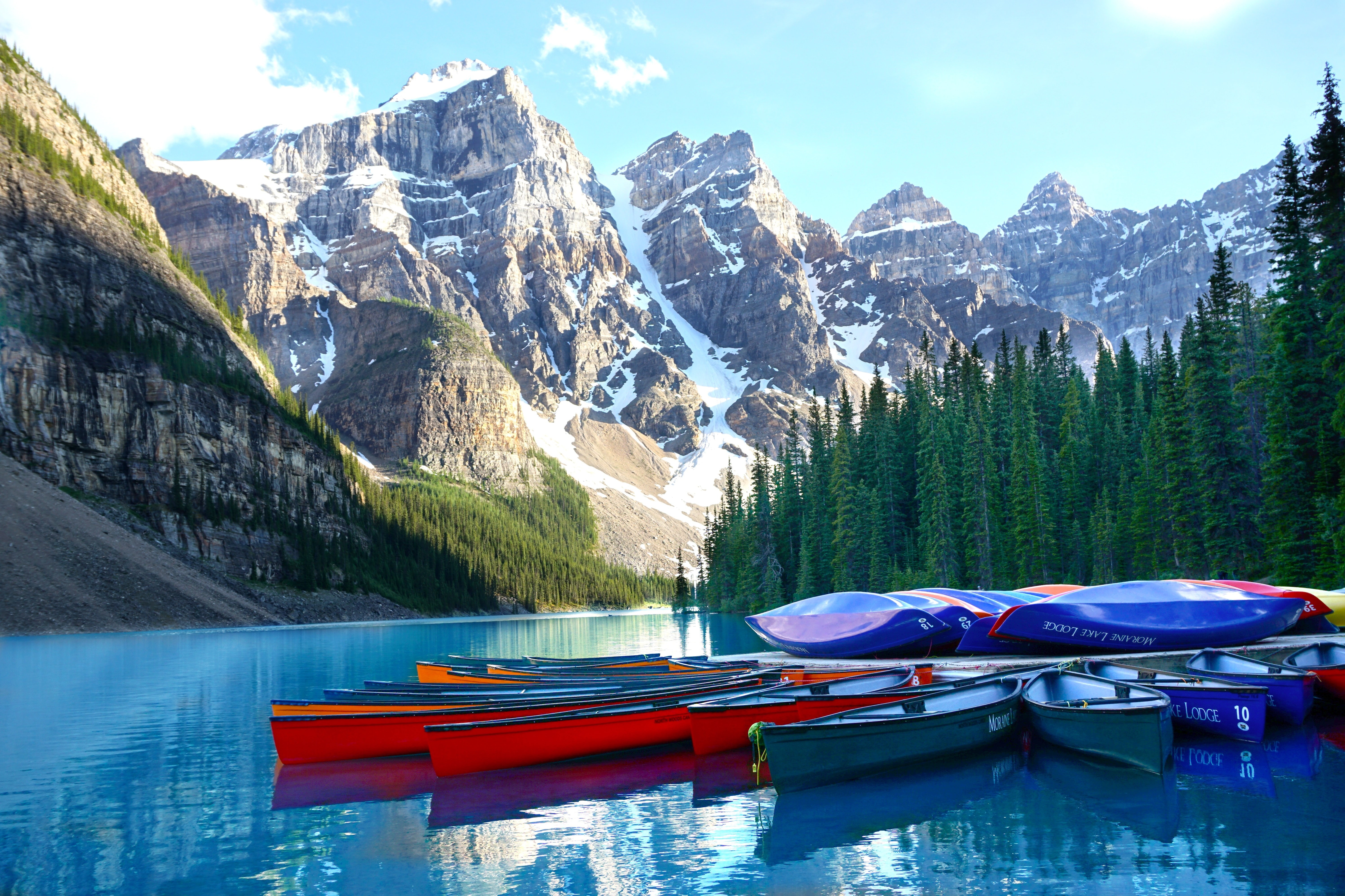 Eine Gruppe von Kanus, die am Lake Louise an einem Steg festgemacht haben, mit Bergen und Bäumen im Hintergrund in Banff, Kanada