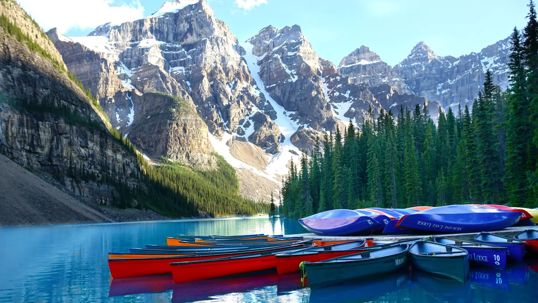 A group of canoes moored up against a dock at Lake Louise with mountains and trees in the background in Banff, Canada