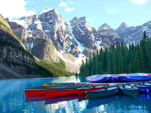 Eine Gruppe von Kanus, die am Lake Louise an einem Steg festgemacht haben, mit Bergen und Bäumen im Hintergrund in Banff, Kanada