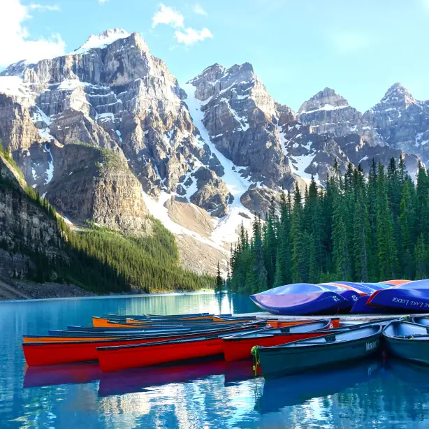 A group of canoes moored up against a dock at Lake Louise with mountains and trees in the background in Banff, Canada