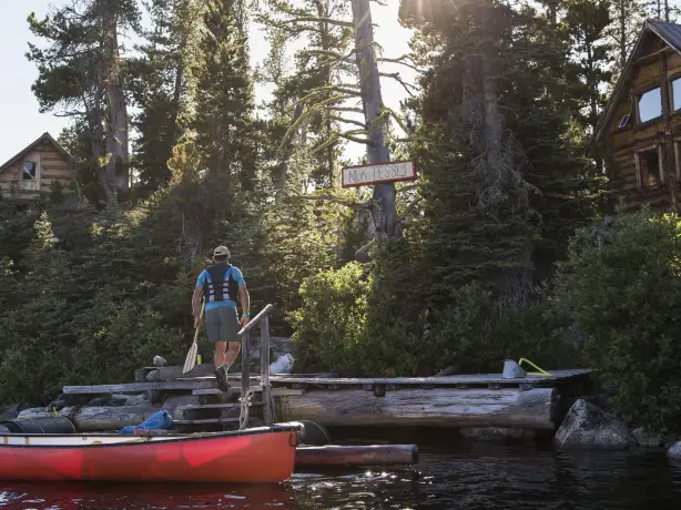 Rotes Kanu an einem Bootssteg vor Blockhütten und Nadelwald an einem ruhigen See in Kanada