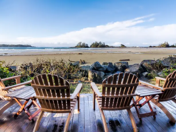 Holzstühle auf einer Terrasse mit Blick auf einen ruhigen Strand und das Meer an der Kanadischen Küste