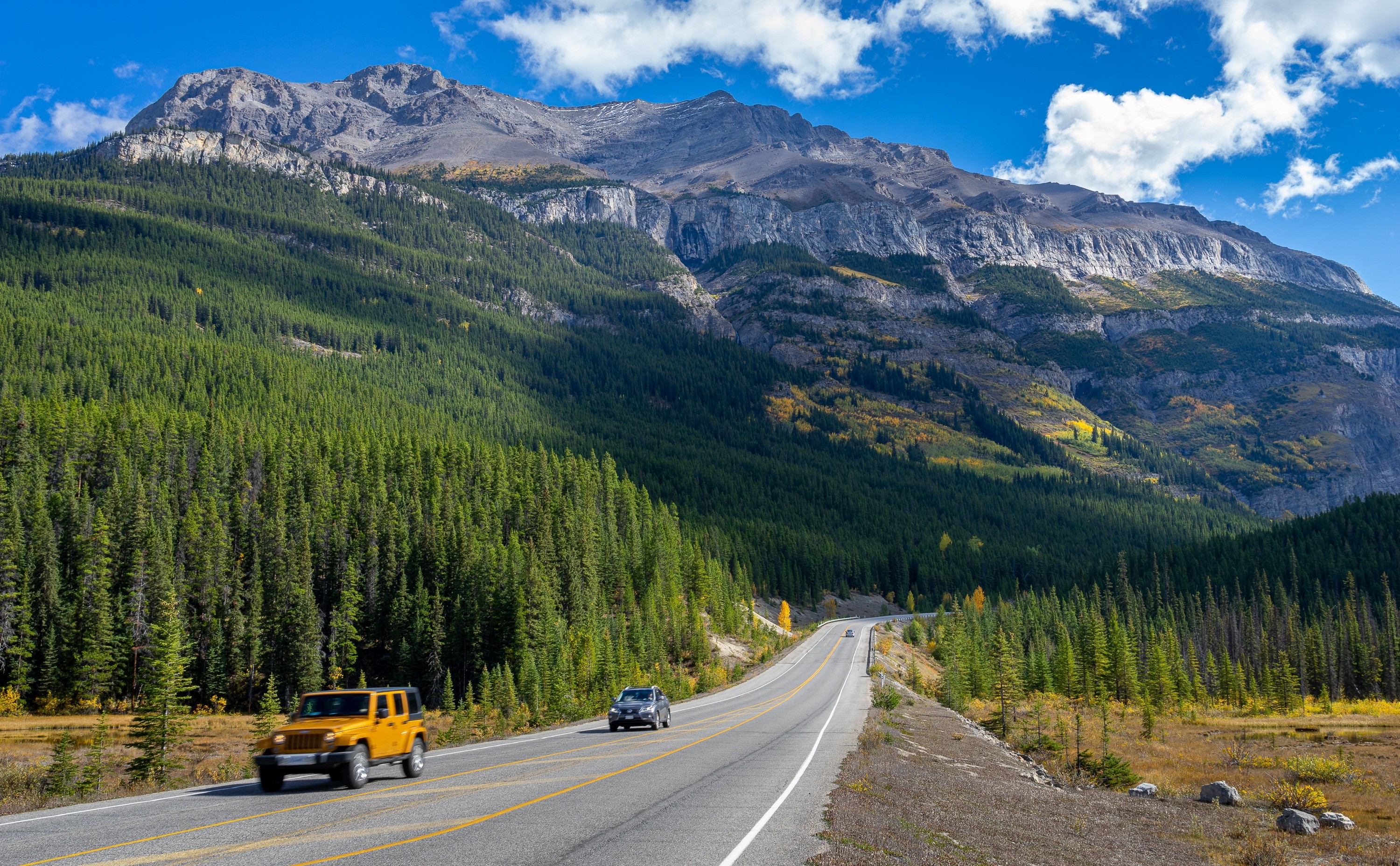 Zwei Autos fahren auf Straße in Kanada mit großen Bergen im Hintergrund