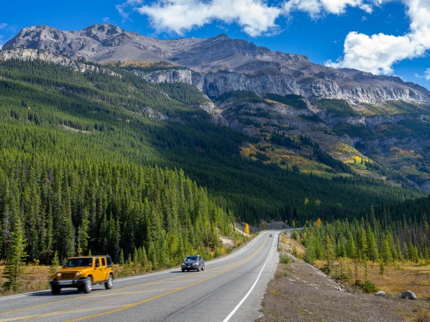 Zwei Autos fahren auf Straße in Kanada mit großen Bergen im Hintergrund