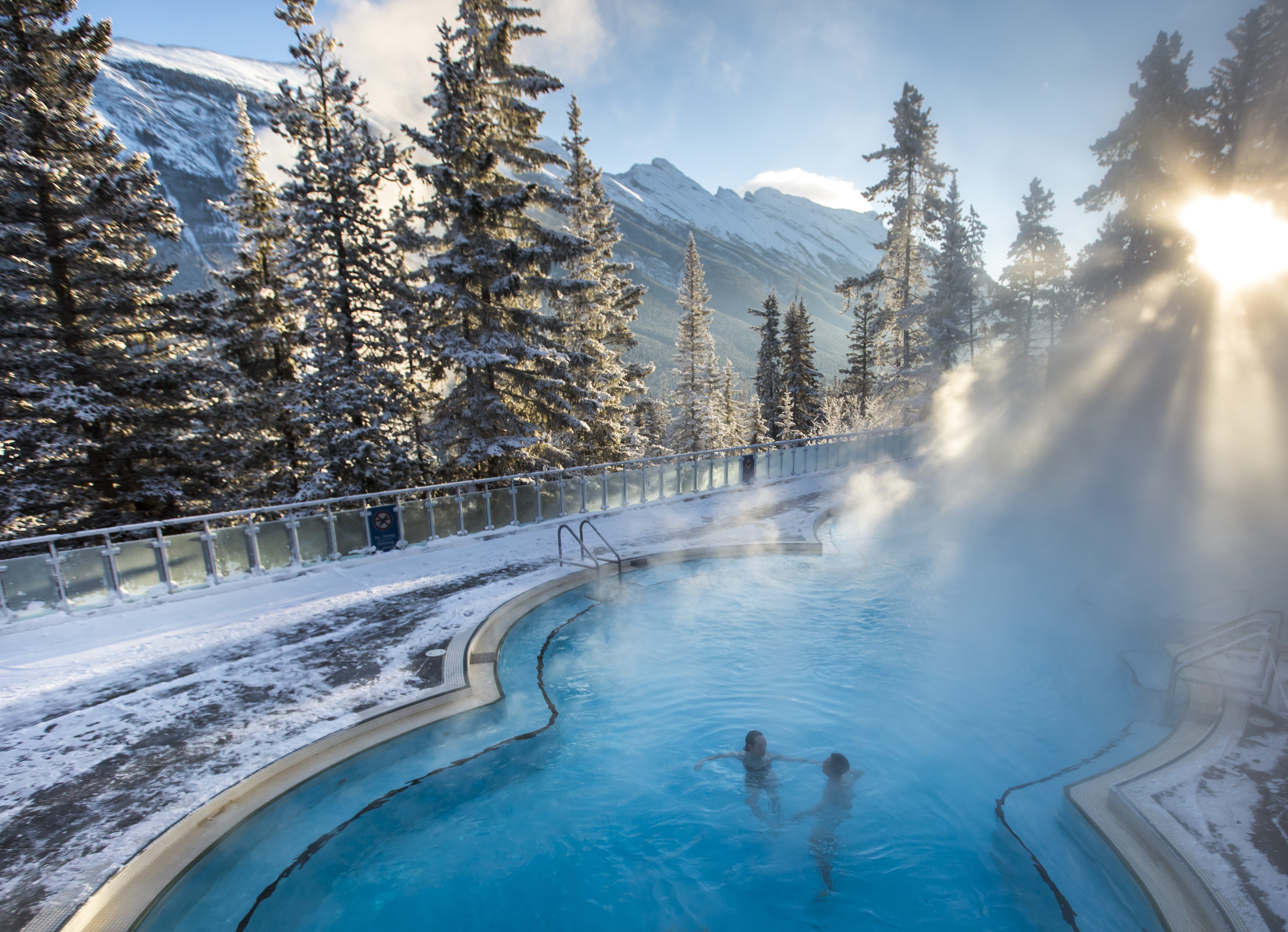 Ein Paar entspannt sich im Winter in Banff, Kanada, in einer heißen Quelle, umgeben von einer verschneiten Landschaft
