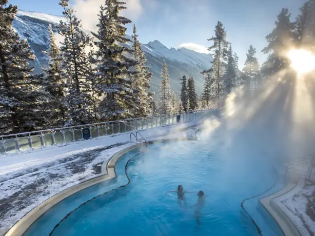 Ein Paar entspannt sich im Winter in Banff, Kanada, in einer heißen Quelle, umgeben von einer verschneiten Landschaft