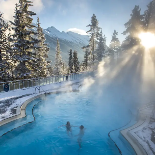 A couple relax in hot spring surrounded by snowy scenery during winter in Banff, Canada