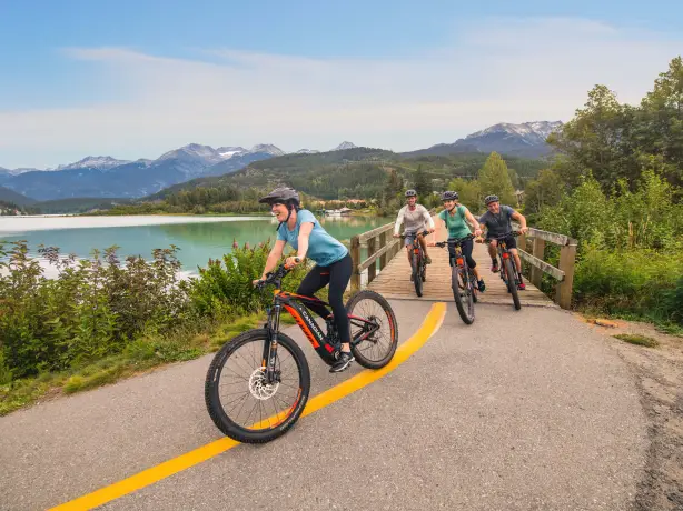 Eine Gruppe, die in Whistler vor der Kulisse von Seen, Wäldern und Bergen Rad fährt