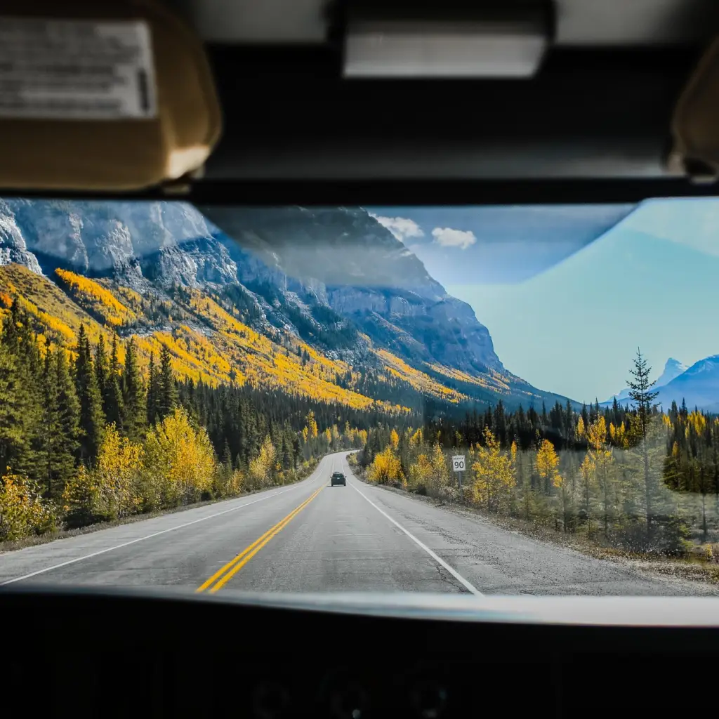 Blick aus der Frontscheibe eines Fahrzeuges auf Straße mit bunten Wäldern und Bergen in Kanada
