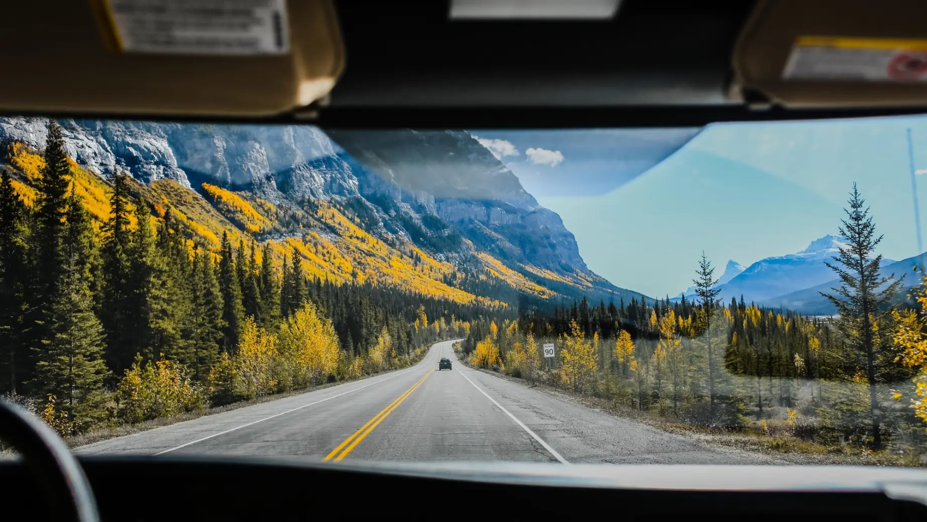 Blick aus der Frontscheibe eines Fahrzeuges auf Straße mit bunten Wäldern und Bergen in Kanada