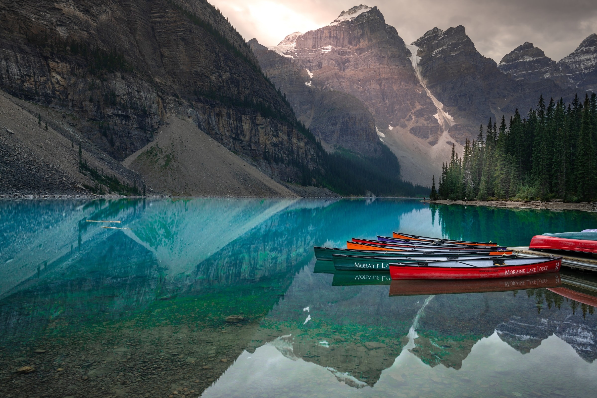 Canoes sit moored by a deck on Moraine Lake in Jasper National Park, Canada, where the surrounding mountains reflect in the water