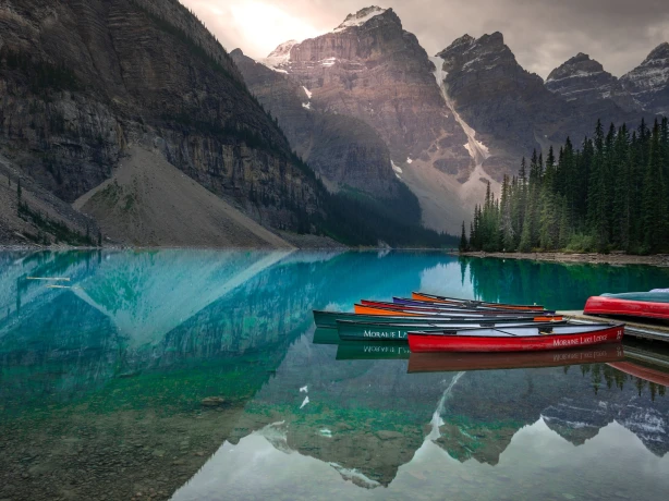 Canoes sit moored by a deck on Moraine Lake in Jasper National Park, Canada, where the surrounding mountains reflect in the water