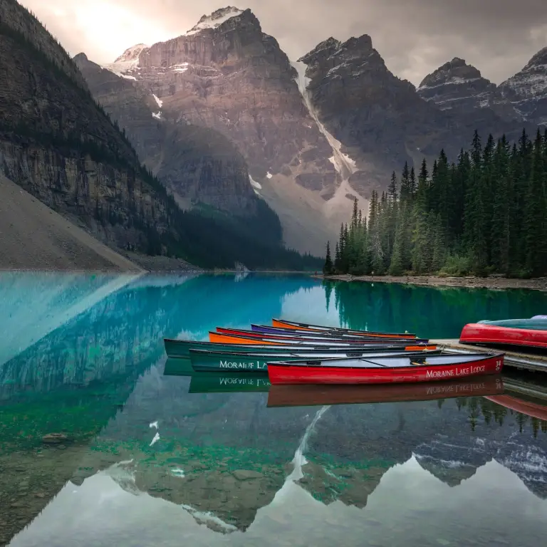 Canoes sit moored by a deck on Moraine Lake in Jasper National Park, Canada, where the surrounding mountains reflect in the water
