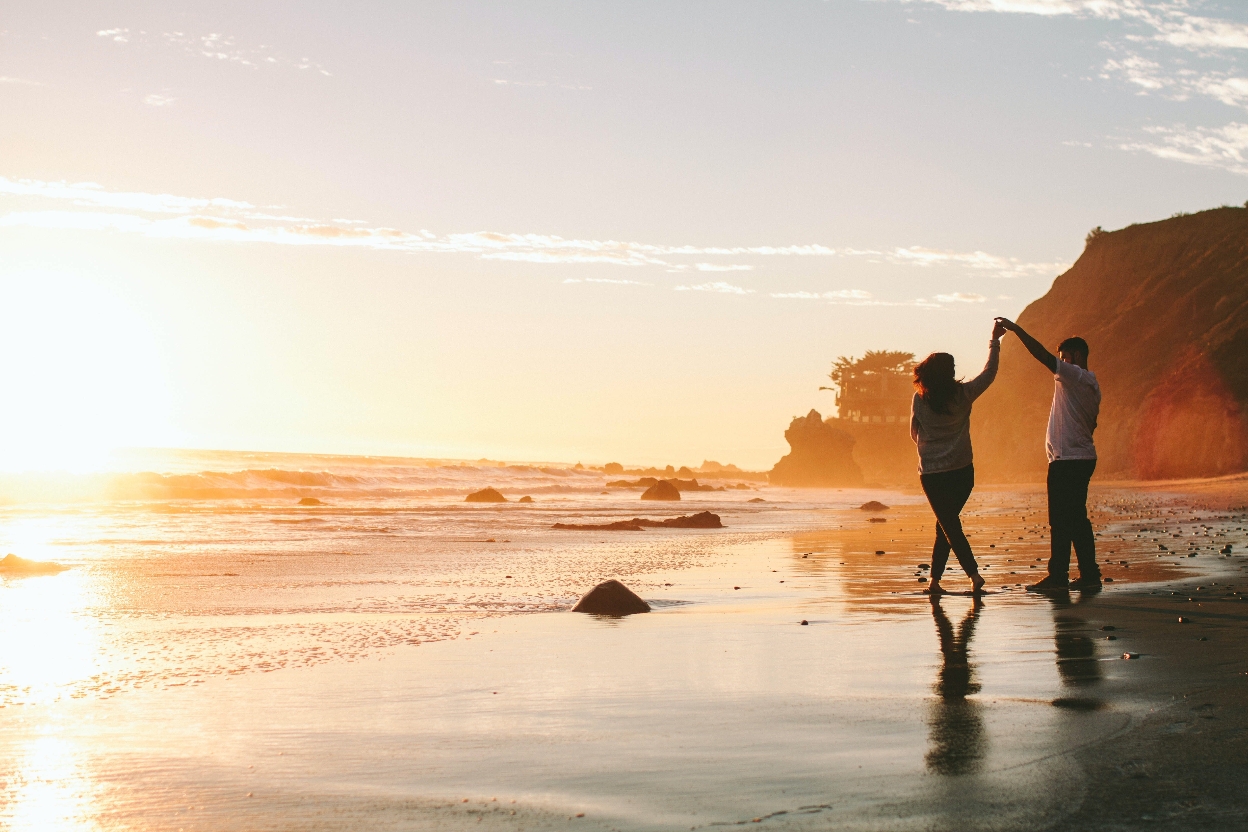 A couple hold hands while walking on the beach during sunset in California, USA
