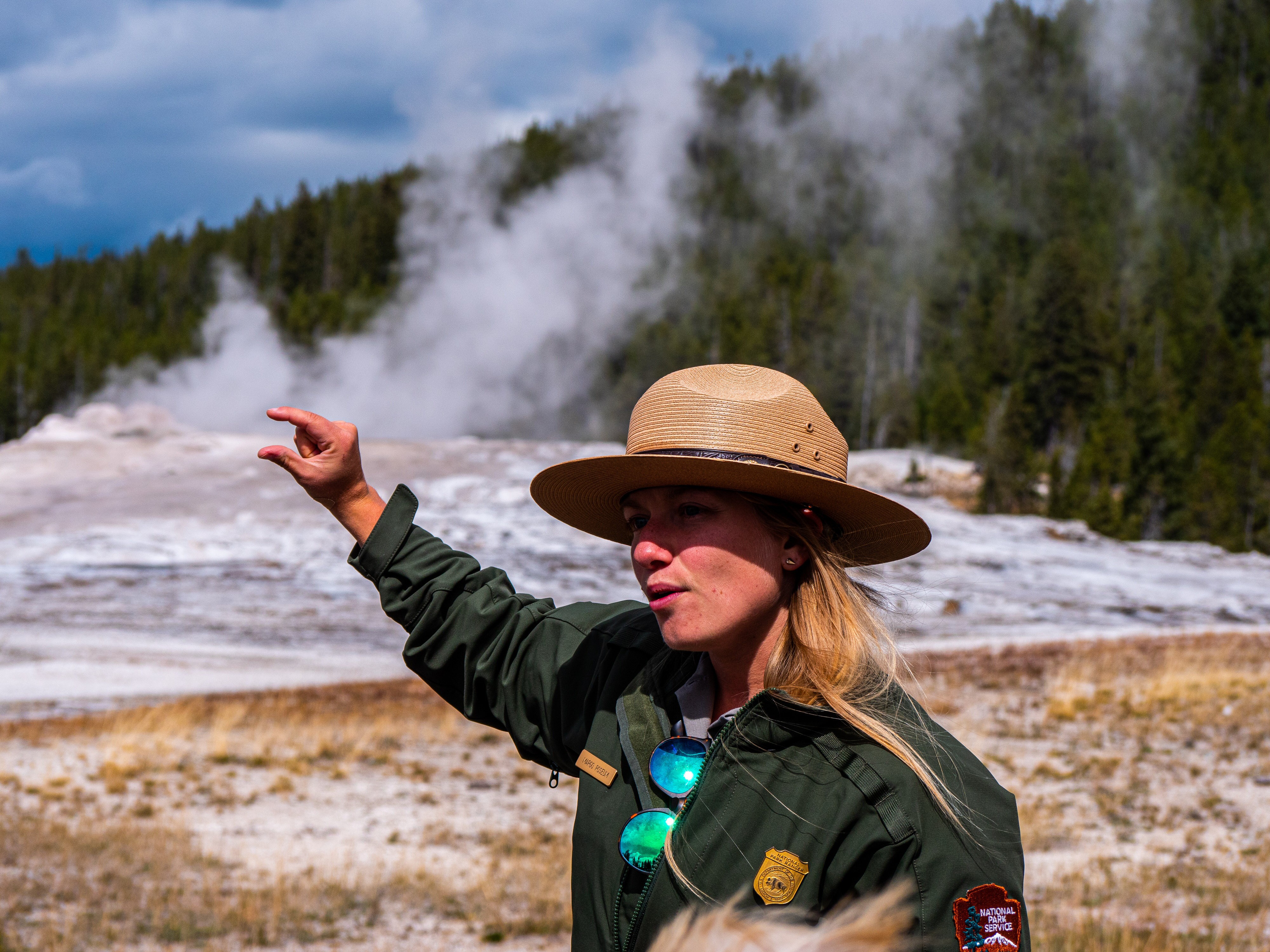 A Yellowstone park ranger gives an explanation to visitors about a geyser in the background