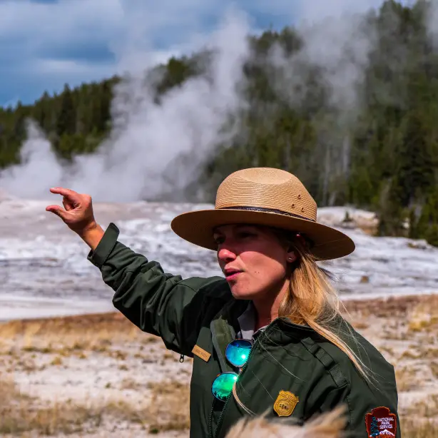 A Yellowstone park ranger gives an explanation to visitors about a geyser in the background