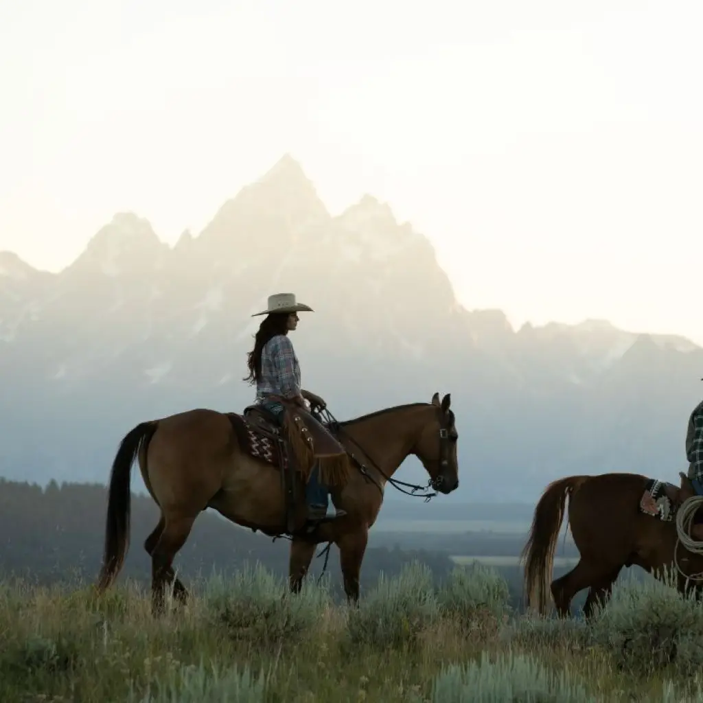 A man and a woman ride horses with a background of mountains in Wyoming, USA