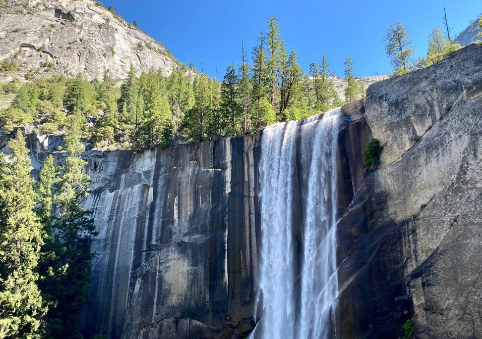 Der Vernal Fall stürzt über eine steile Granitklippe im Yosemite National Park, umgeben von hohen Kiefern und hellem Berglicht.