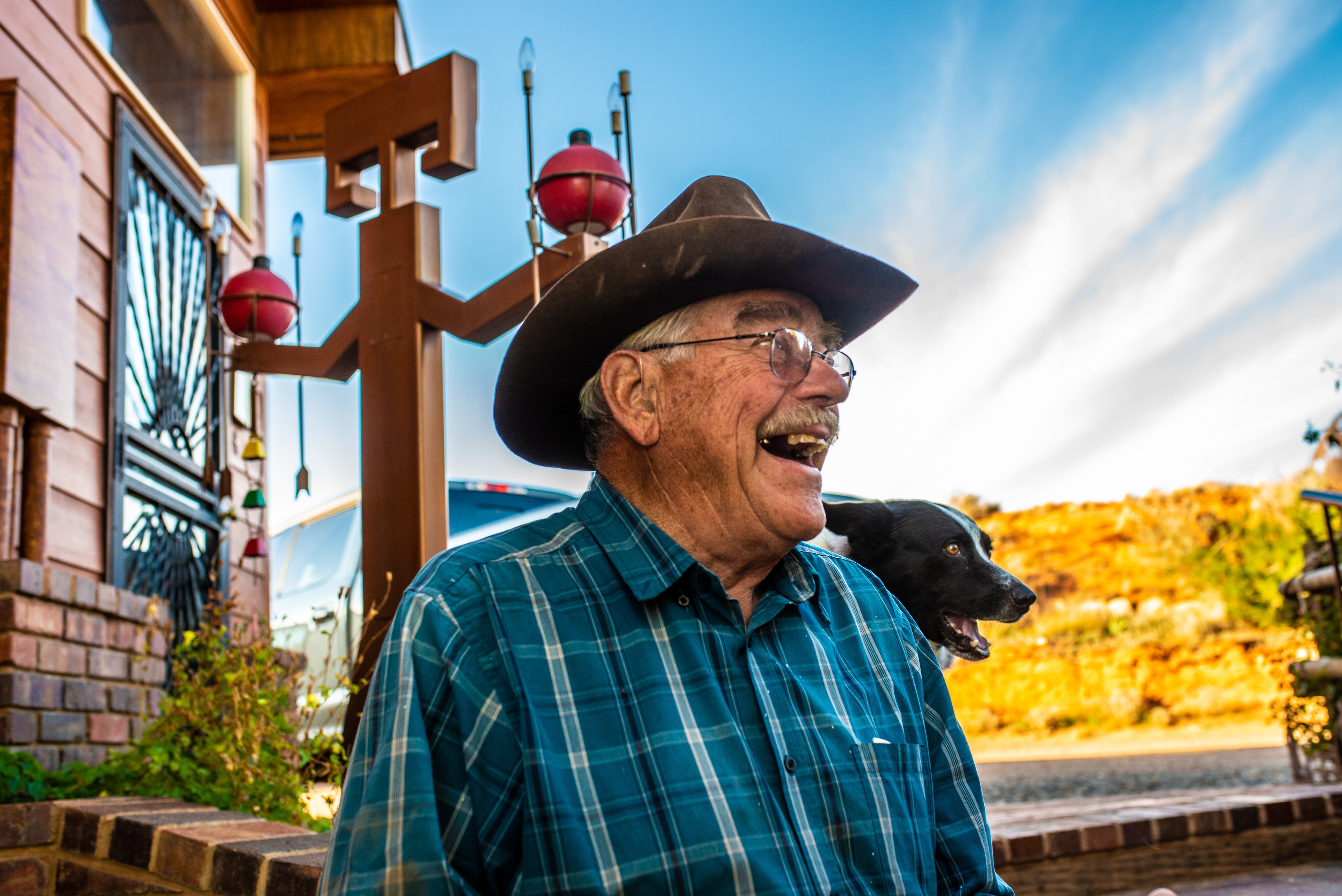 Der pensionierte Cowboy und Besitzer einer Gäste-Ranch Jerry Kinknade schaut nach rechts von der Kamera und lächelt, sein Hund und seine Ranch sind hinter ihm zu sehen.