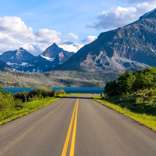 Een open weg die leidt naar de bergen en het meer in Glacier National Park, Montana, VS, onder een heldere zomerhemel.