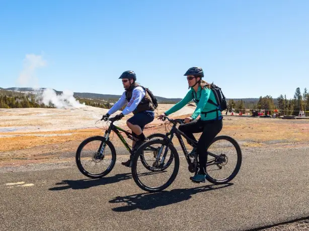 Zwei Menschen fahren mit dem Fahrrad an einem dampfenden Geysir im Yellowstone-Nationalpark in den USA vorbei