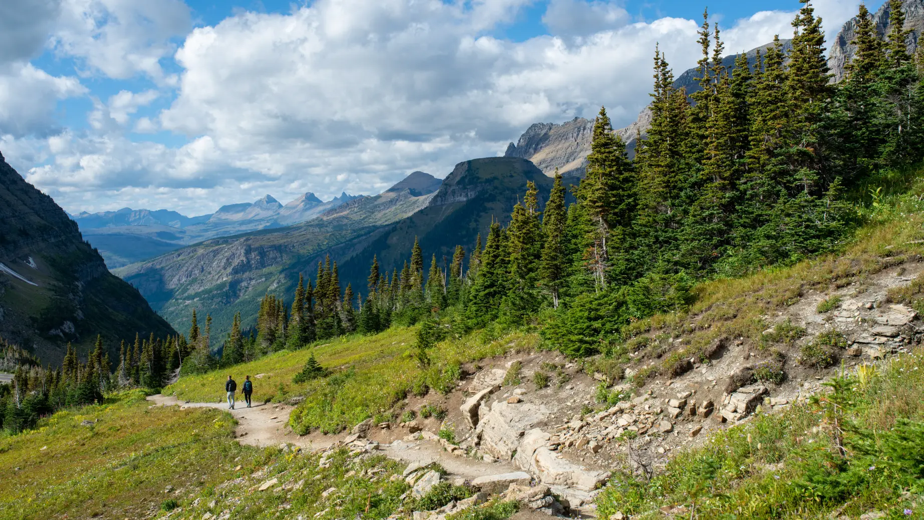 Couple hiking trail surrounded by mountains in Glacier National Park