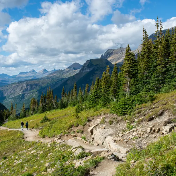 Couple hiking trail surrounded by mountains in Glacier National Park