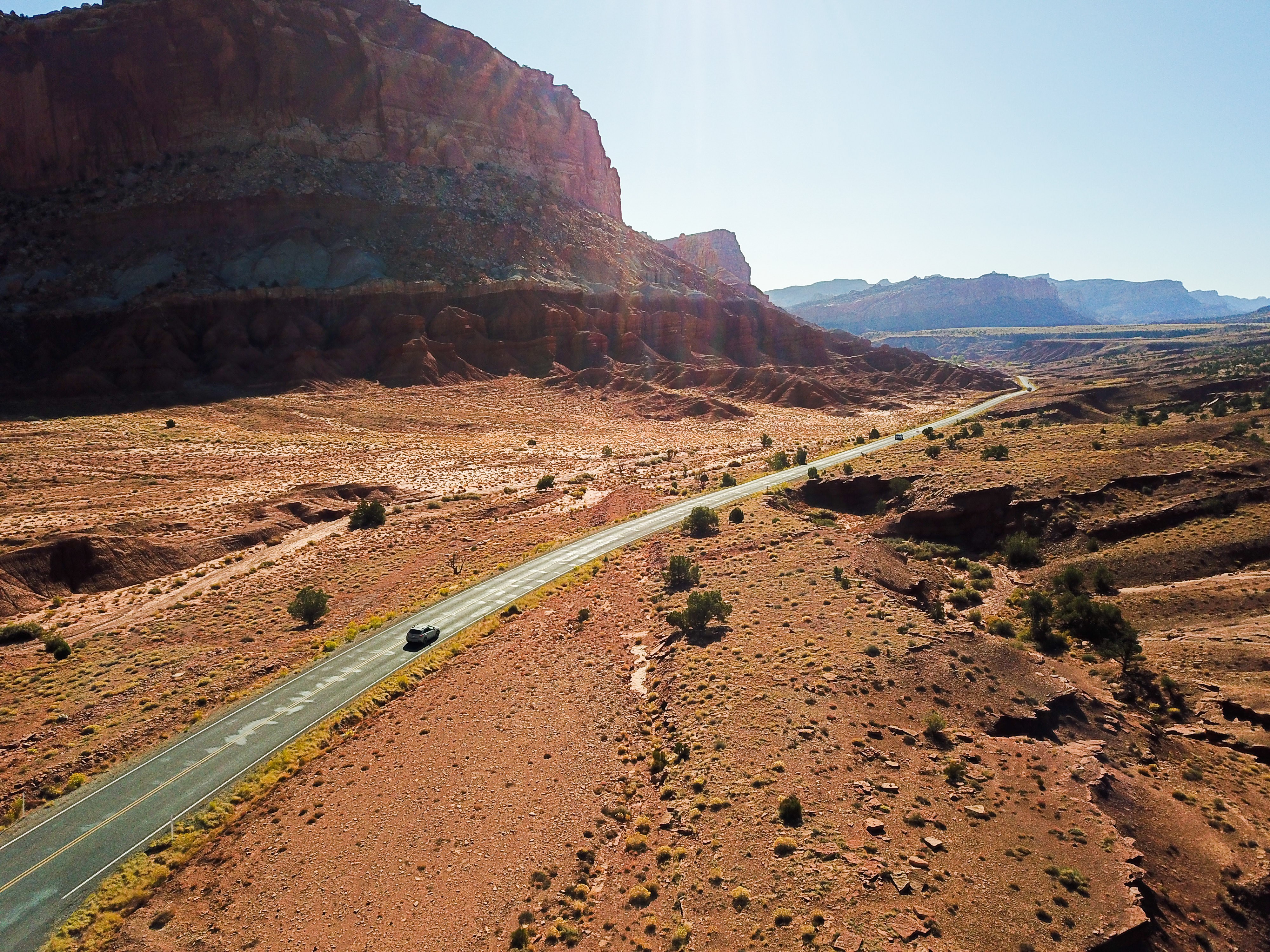 Ein Auto fährt auf einem abgelegenen Wüsten-Highway in Utah, umgeben von roten Felsen und weiten Landschaften.