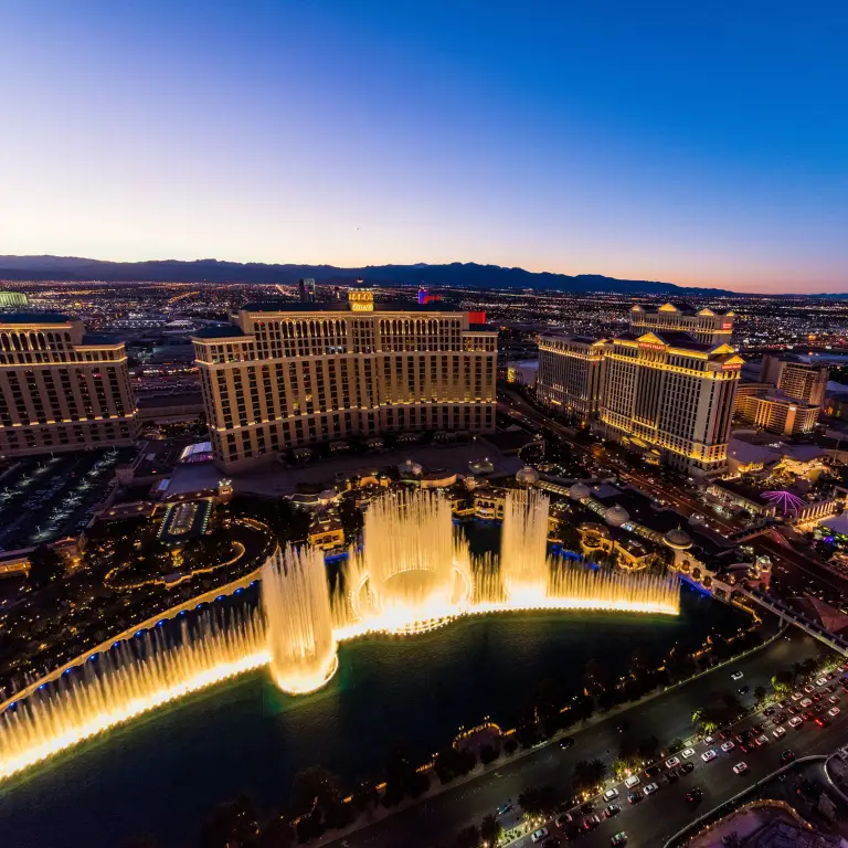Luchtfoto van de Bellagio-fonteinen in de avond in Las Vegas met stadsverlichting, verkeer en bergen op de achtergrond