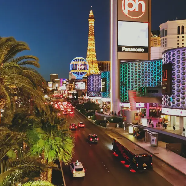 Levendig avondbeeld van Las Vegas met verlichte gebouwen, palmbomen, druk verkeer en de iconische Eiffeltoren-replica
