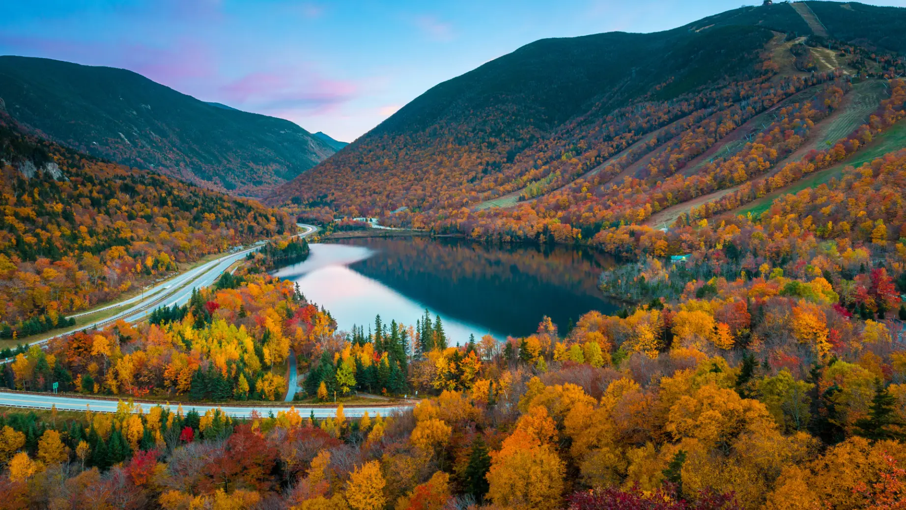 Autumnal foliage around a lake and road in New England, USA