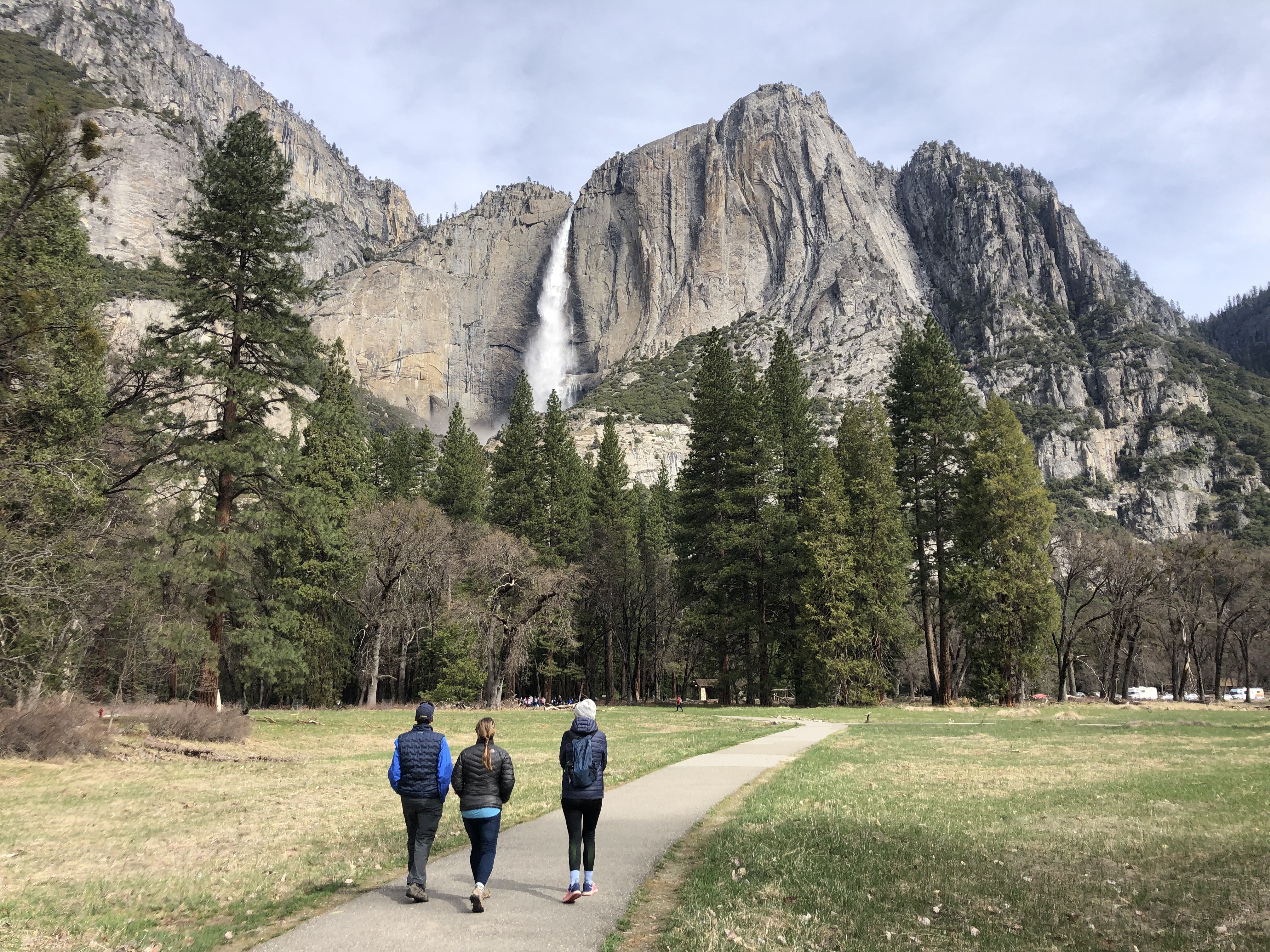 Drei Menschen wandern durch Yosemite Tal mit Berg und Wasserfall im Hintergrund